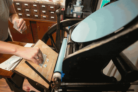 A hand feeding small printed cards one at a time through a hand-operated letterpress