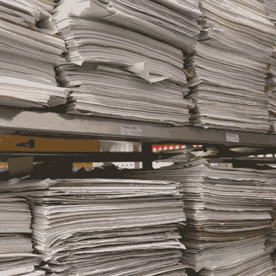 Floor to ceiling metal shelving packed with tall, leaning stacks of loose paper files